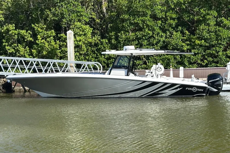  Yacht Photos Pics 2022 Fountain 38 CC LS boat docked on calm water, surrounded by lush greenery.