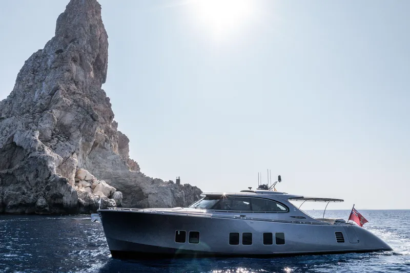 Loloma Yacht Photos Pics 2025 Zeelander 7 yacht cruising near a rocky cliff under a bright sun.