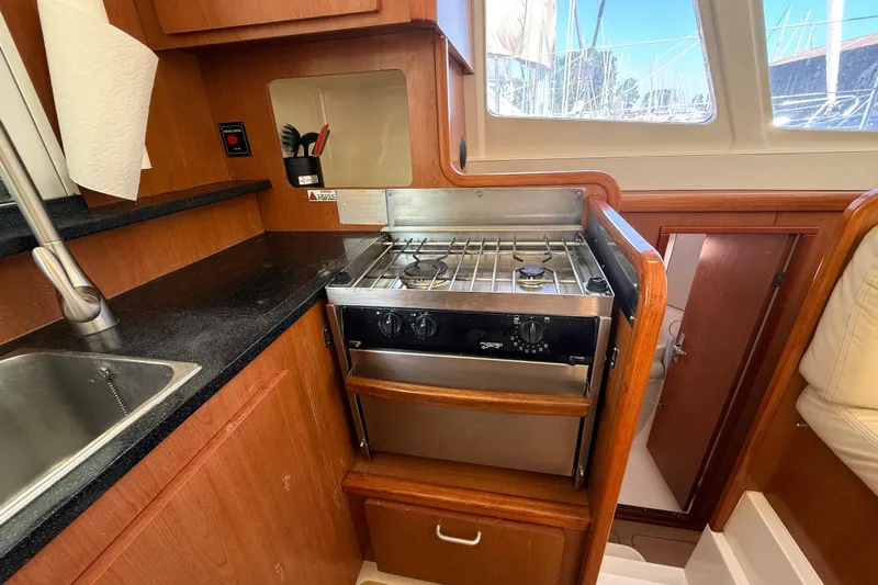Selah Yacht Photos Pics Compact kitchen in a 2010 Leopard 38 yacht with stove, sink, and wooden cabinetry.