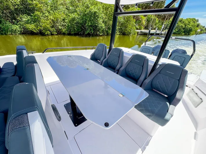  Yacht Photos Pics 2024 Axopar 37 Sun Top boat with sleek seating and table, surrounded by lush greenery.