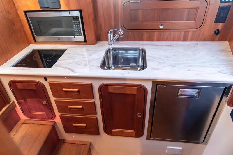 Leodes Yacht Photos Pics 2022 Hinckley Picnic Boat 34 S galley with sink, microwave, and wooden cabinetry.