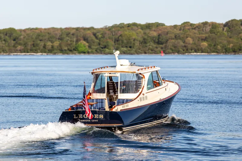 Leodes Yacht Photos Pics 2022 Hinckley Picnic Boat 34 S cruising on a serene lake with lush green shoreline.