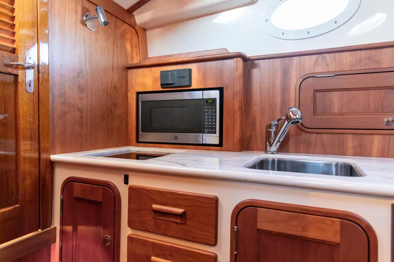 Leodes Yacht Photos Pics 2022 Hinckley Picnic Boat 34 S interior kitchen with wood cabinetry, microwave, and sink.