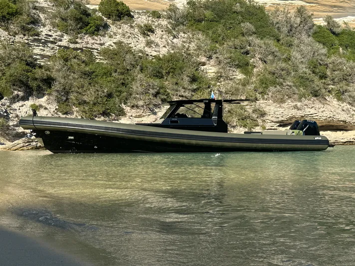 Nomad Yacht Photos Pics 2023 Sea Water PHANTOM 500 boat anchored near rocky shoreline with lush greenery.