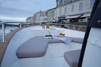2026 Rhea 27 Open V2 boat with cozy seating, docked by historic waterfront buildings.