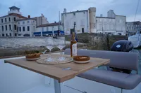Rhea 27 Open V2 boat with wine and snacks on table, docked by historic buildings.