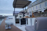 Rhea 27 Open V2 boat interior with seating, table, and canopy, docked by waterfront buildings.