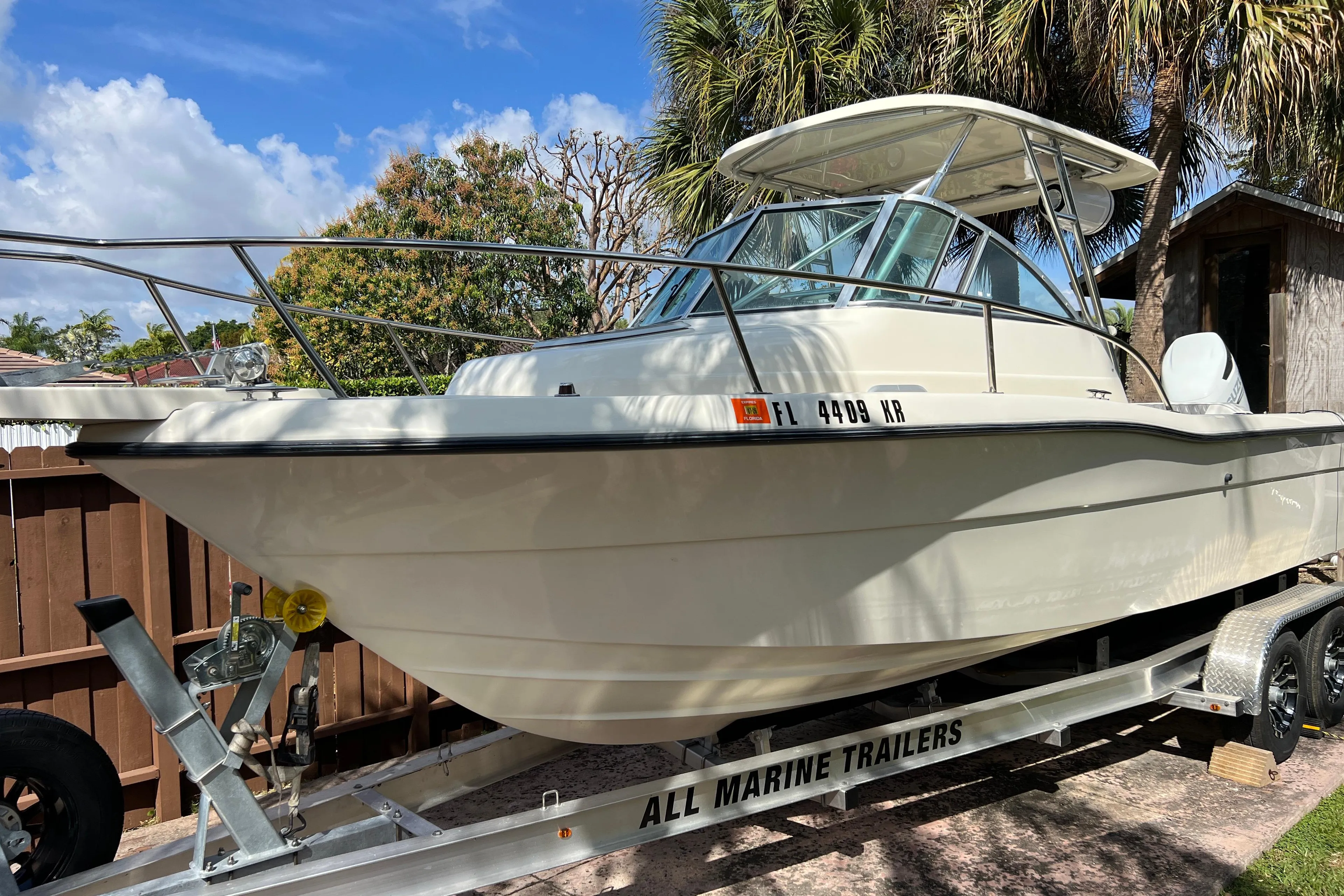 1999 Pursuit 2470 Walkaround boat on trailer, surrounded by palm trees.