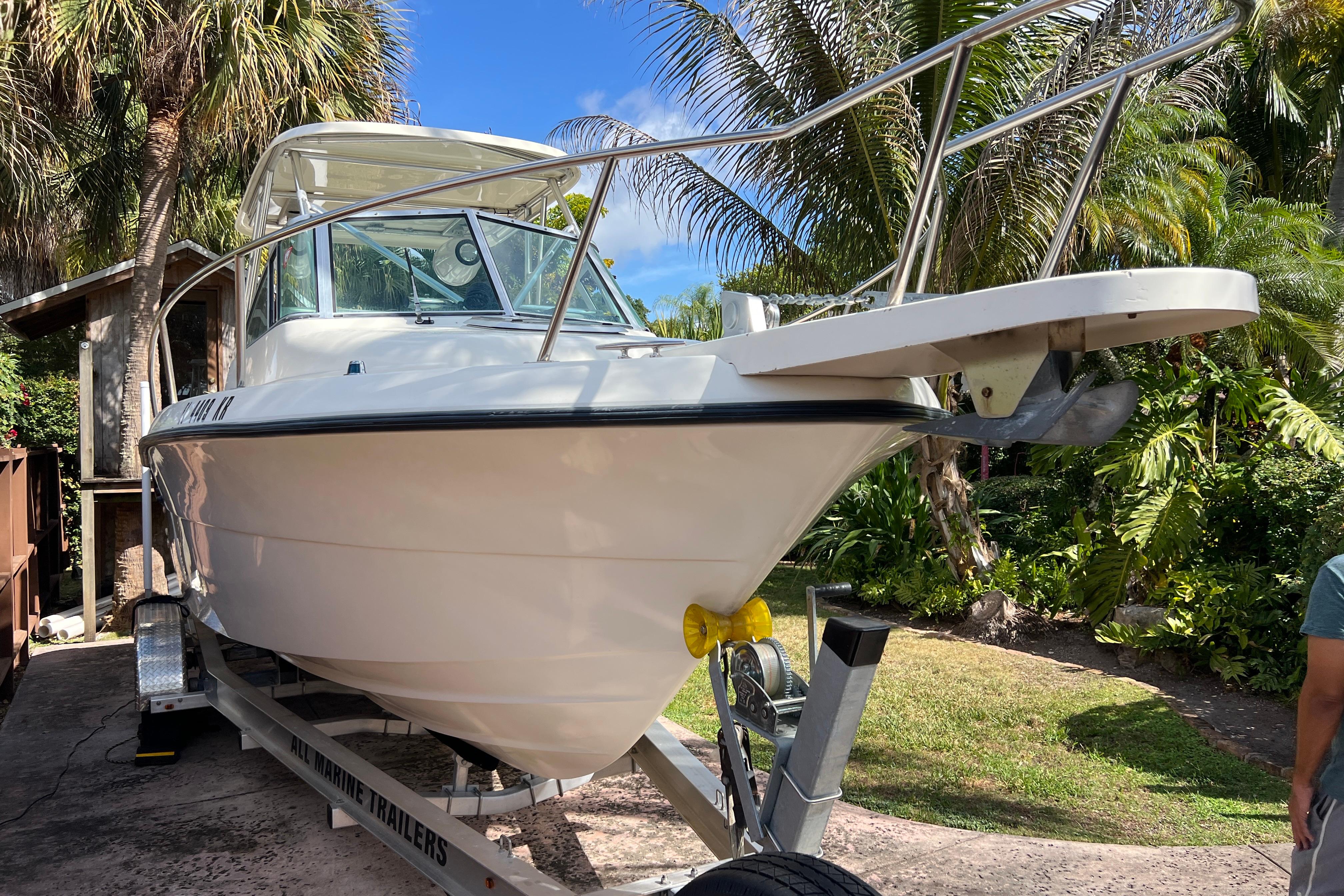 1999 Pursuit 2470 Walkaround boat on trailer, surrounded by tropical foliage.