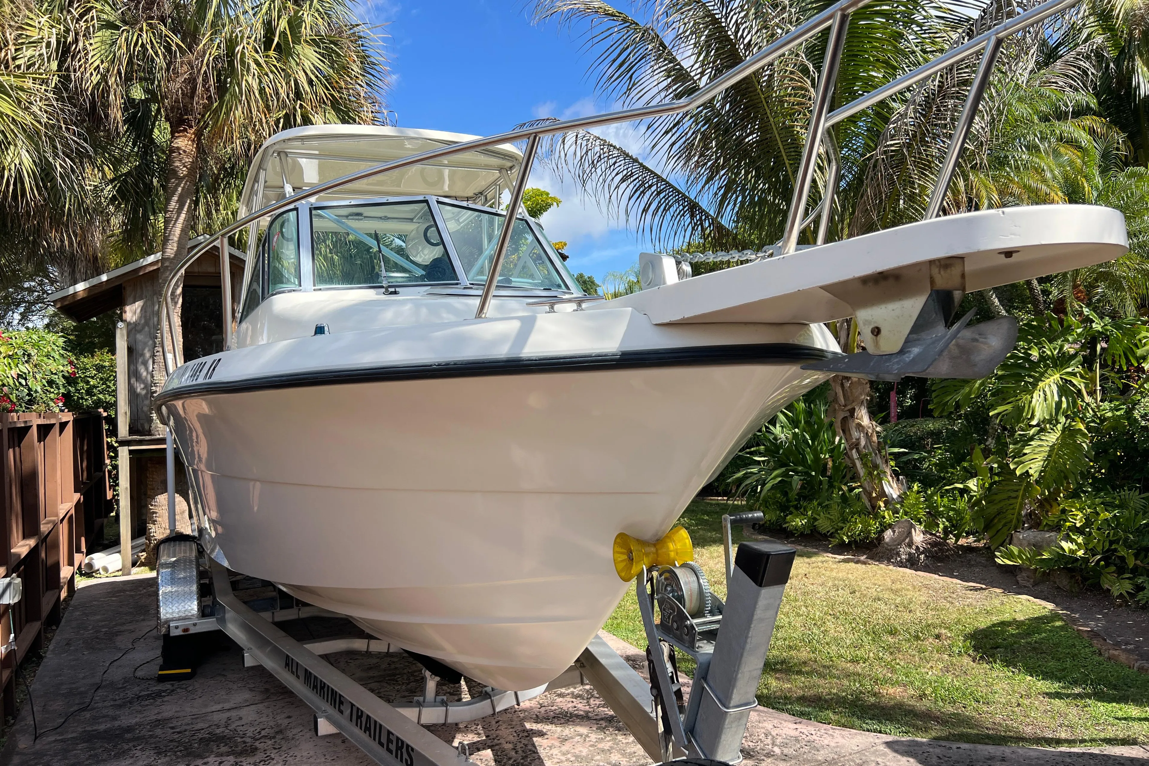 1999 Pursuit 2470 Walkaround boat on trailer, surrounded by tropical foliage.