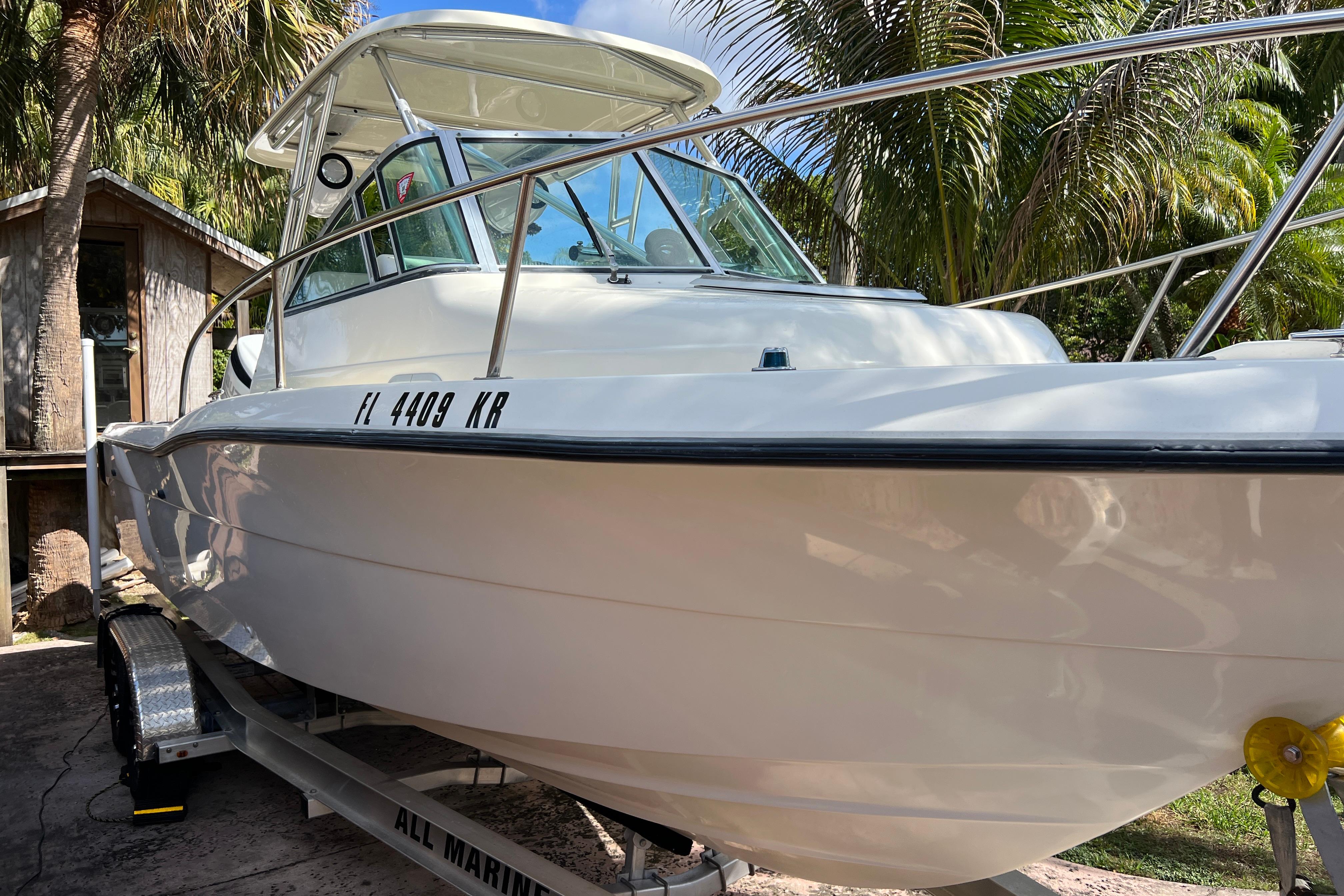 1999 Pursuit 2470 Walkaround boat on trailer, surrounded by palm trees.