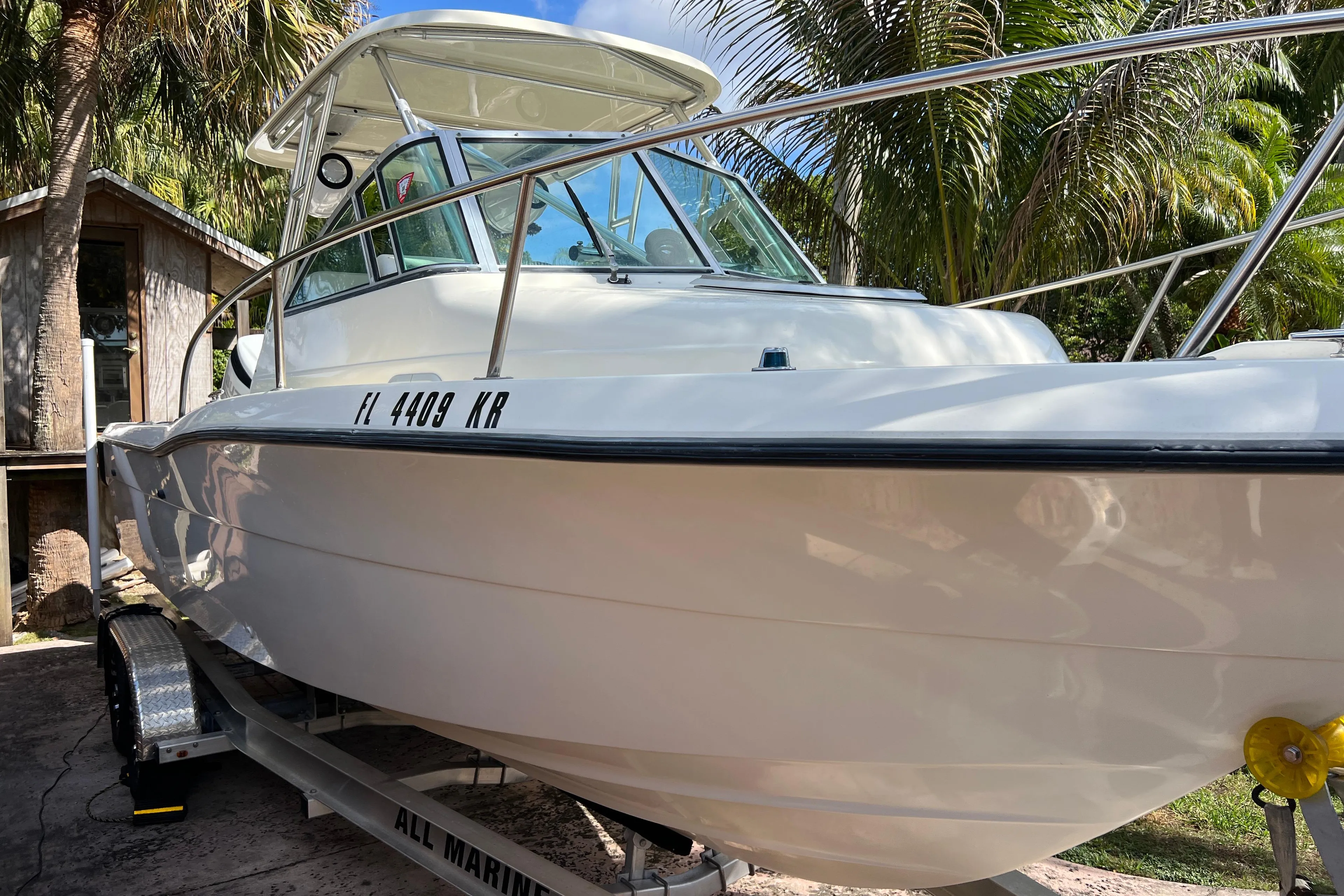 1999 Pursuit 2470 Walkaround boat on trailer, surrounded by palm trees.