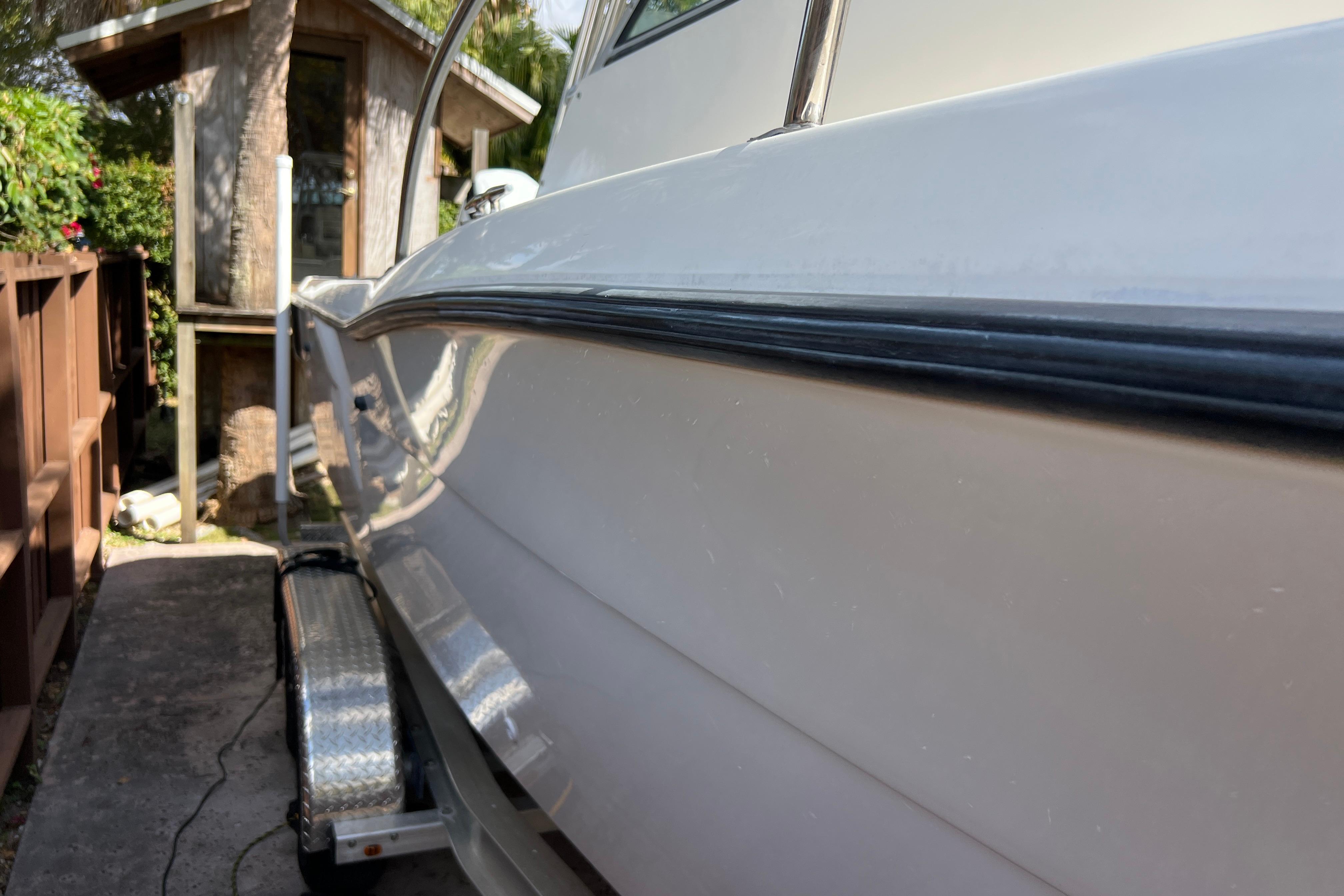 1999 Pursuit 2470 Walkaround boat on trailer beside wooden fence and small shed.