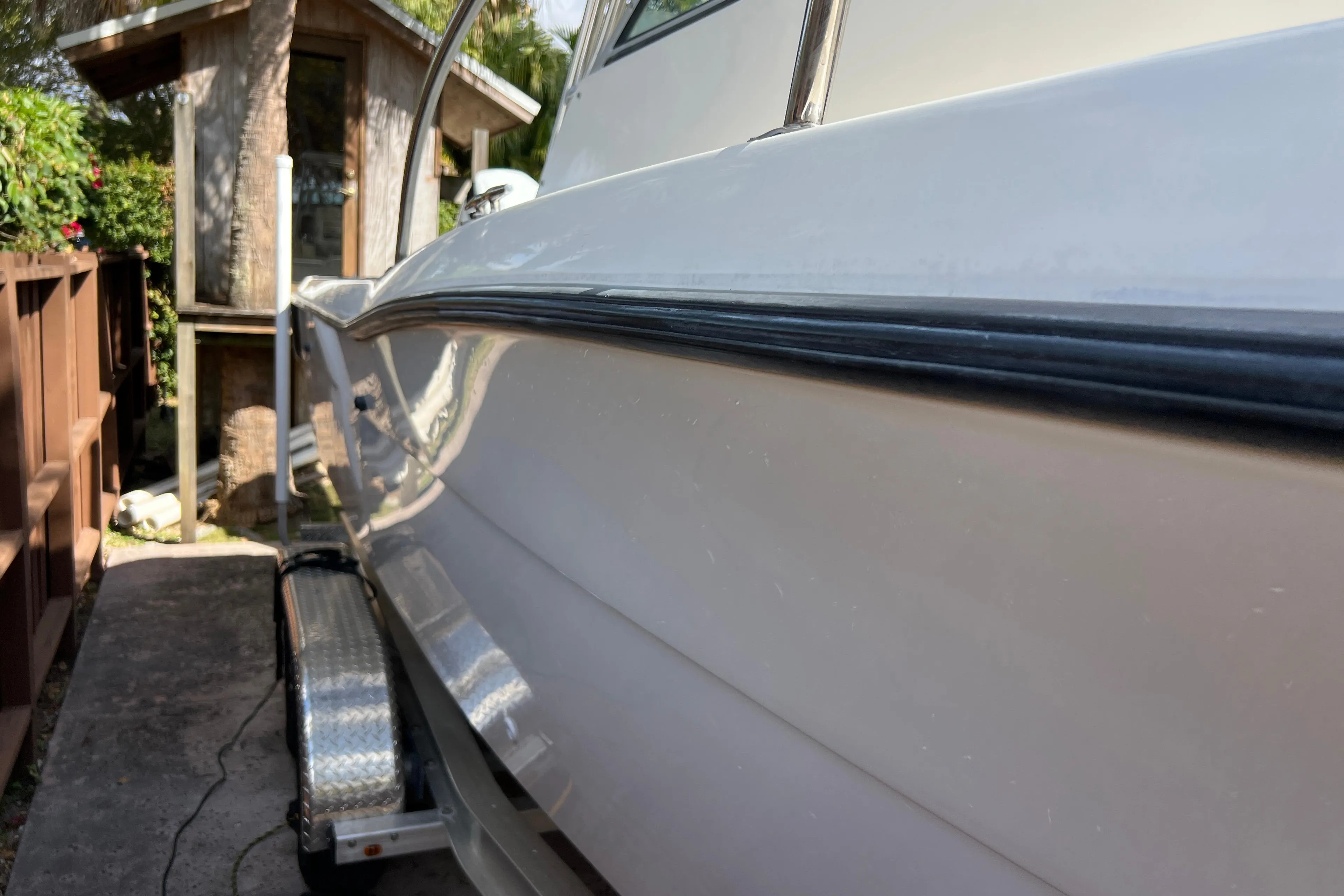 1999 Pursuit 2470 Walkaround boat on trailer beside wooden fence and small shed.