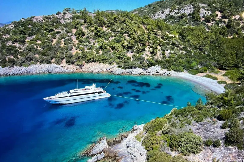 Axella Yacht Photos Pics Luxurious 1991 Crestitalia 33m yacht anchored in a serene, turquoise bay surrounded by lush greenery.