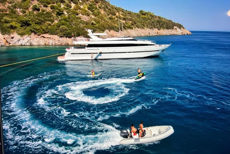 Axella Yacht Photos Pics Luxurious 1991 Crestitalia 33m yacht anchored near scenic coastline with jet skis and small boat.