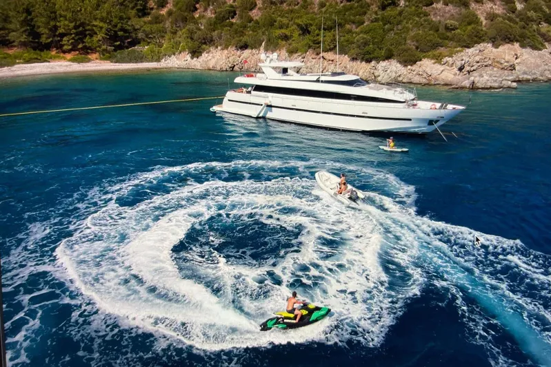 Axella Yacht Photos Pics Luxurious 1991 Crestitalia 33m yacht anchored near scenic coastline with jet skis and boats.