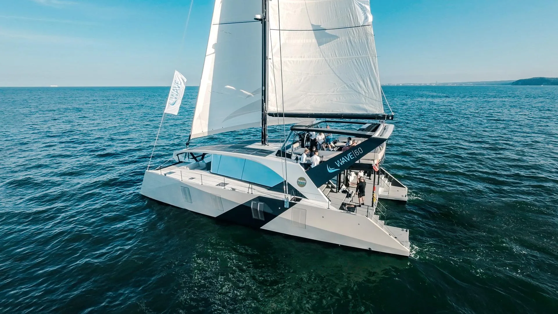 2024 Wave 60 catamaran sailing on open sea under clear blue sky.