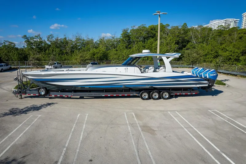  Yacht Photos Pics 2023 MTI 50v boat on trailer in parking lot, surrounded by trees and clear sky.