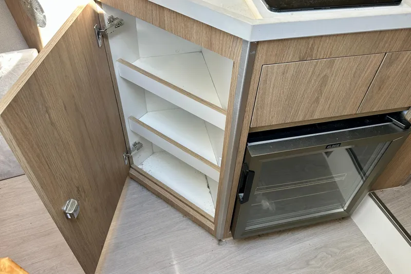  Yacht Photos Pics Open wooden cabinet with shelves beside a compact refrigerator in a 2024 NX 360 Sport Coupe.
