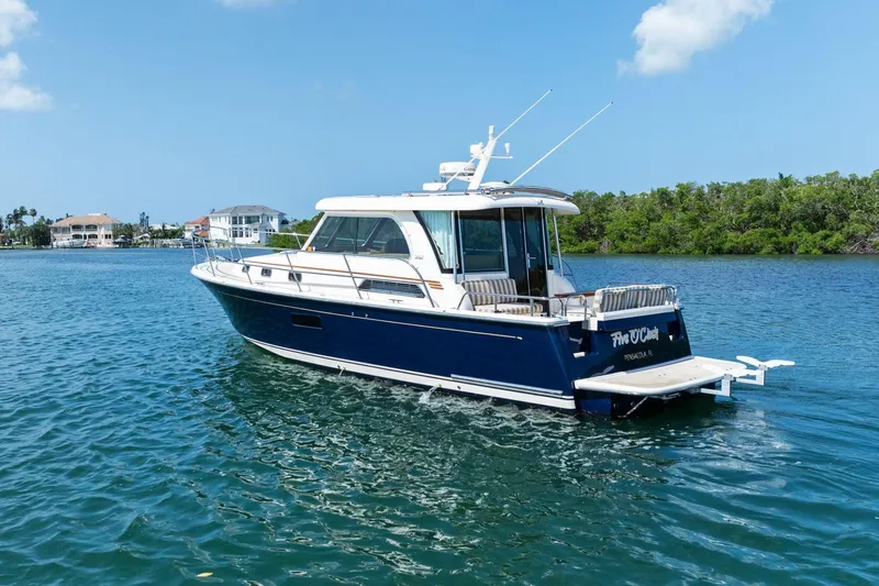 Five O'clock Yacht Photos Pics 2013 Sabre 38 Salon Express yacht cruising on clear blue water near lush shoreline.