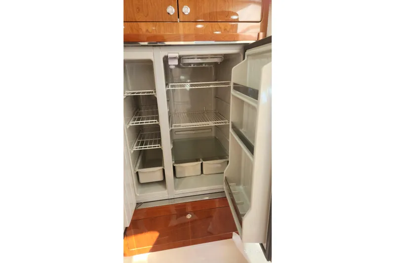  Yacht Photos Pics Open refrigerator inside 2017 Intrepid 475 Sport Yacht, featuring wooden cabinetry and spacious shelving.