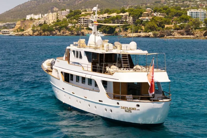 Daylami Yacht Photos Pics 1972 Benetti Yachts Classic cruising in scenic coastal waters, with lush greenery and buildings in the background.