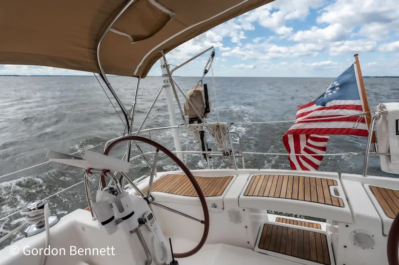 Queens Share Yacht Photos Pics Beneteau Oceanis 43 sailboat deck with American flag, cruising on open water.