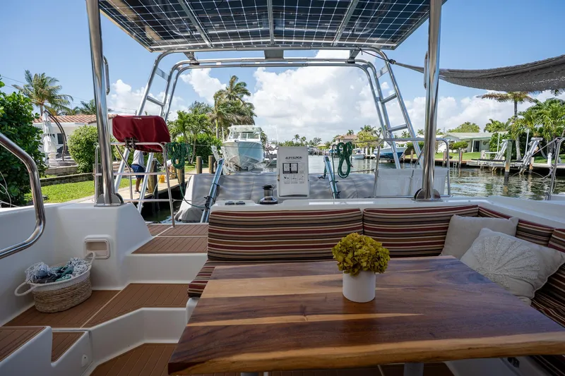  Yacht Photos Pics Lagoon 420 catamaran cockpit with wooden table, striped seating, and solar panels, docked in a marina.