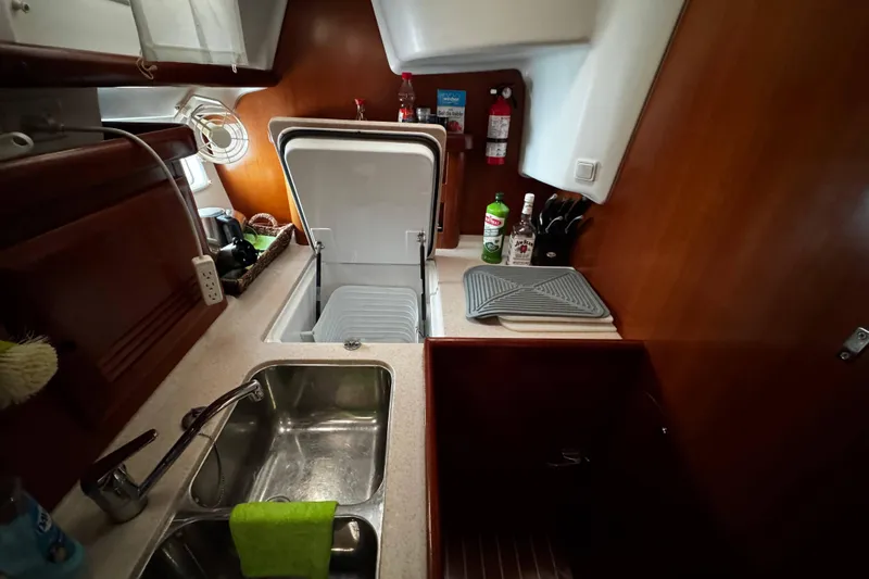 Still In The Moment Yacht Photos Pics Galley kitchen in 2007 Beneteau 423 sailboat with sink, open fridge, and wooden cabinetry.