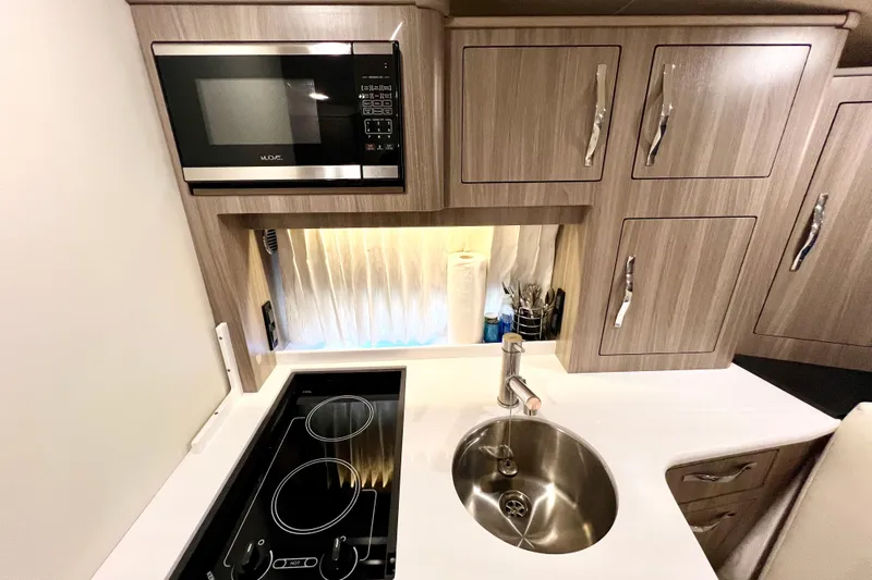 Aventuras Yacht Photos Pics 2021 Regal 33 XO yacht kitchen with microwave, stove, sink, and wooden cabinets.