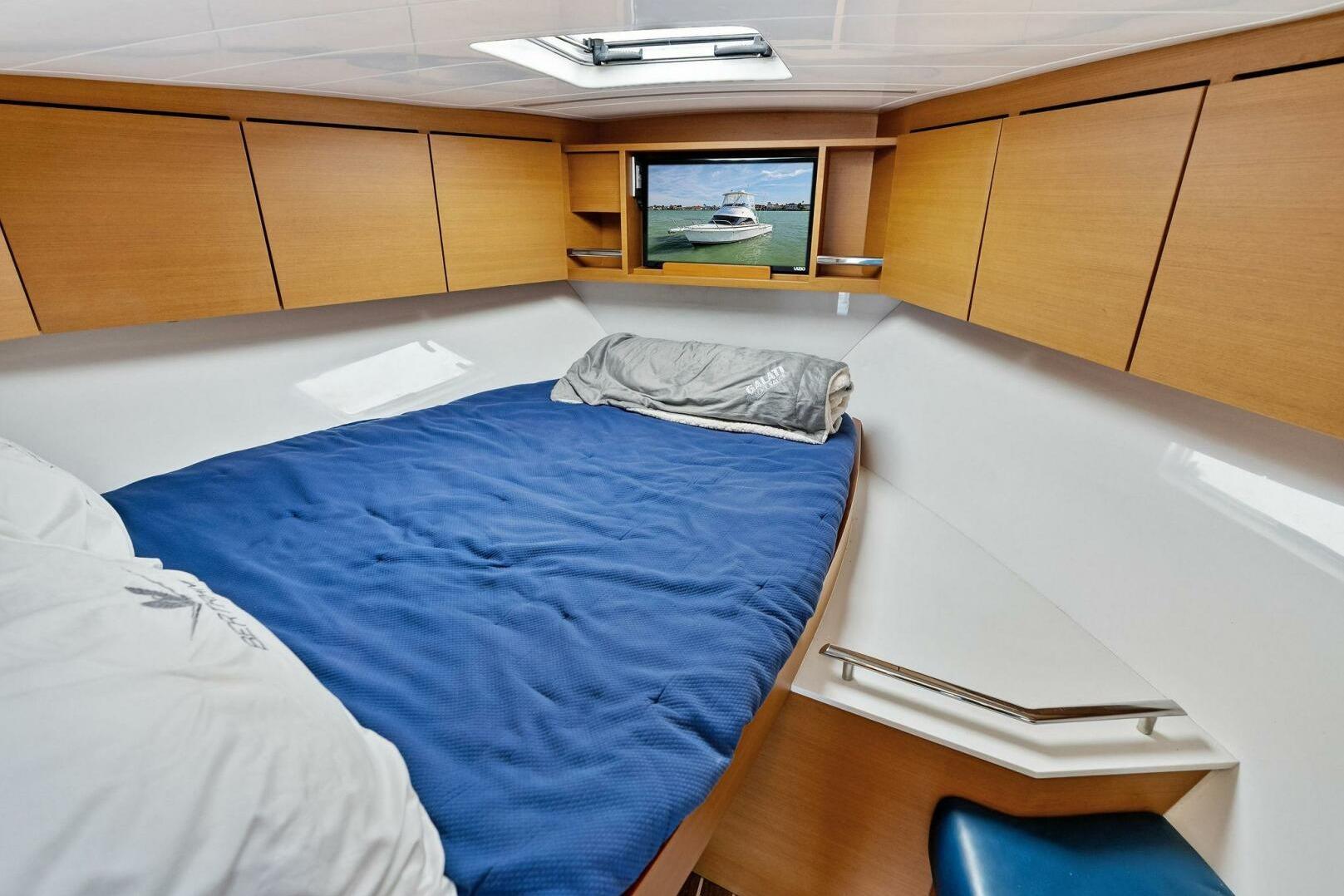 2017 Bertram 35 Flybridge cabin with blue bedding and wooden storage cabinets.