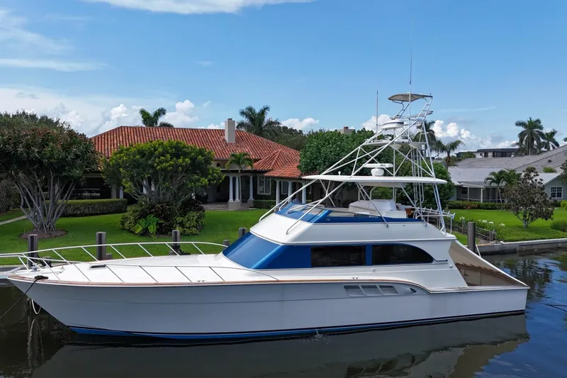 Andiamo Yacht Photos Pics 1991 Donzi 65 Sportfisher yacht docked by a waterfront home, under a clear blue sky.