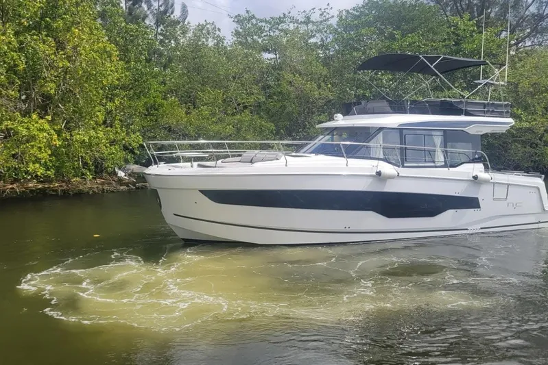 Rhapsody In Sea Yacht Photos Pics 2025 Jeanneau NC 1295 Fly yacht cruising on a calm river surrounded by lush greenery.