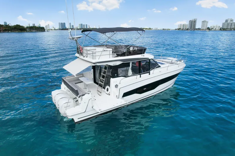 Rhapsody In Sea Yacht Photos Pics 2025 Jeanneau NC 1295 Fly yacht on clear blue water with city skyline.