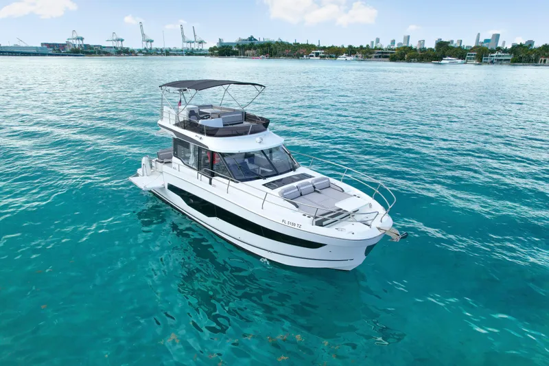 Rhapsody In Sea Yacht Photos Pics 2025 Jeanneau NC 1295 Fly yacht on clear blue water, city skyline in background.
