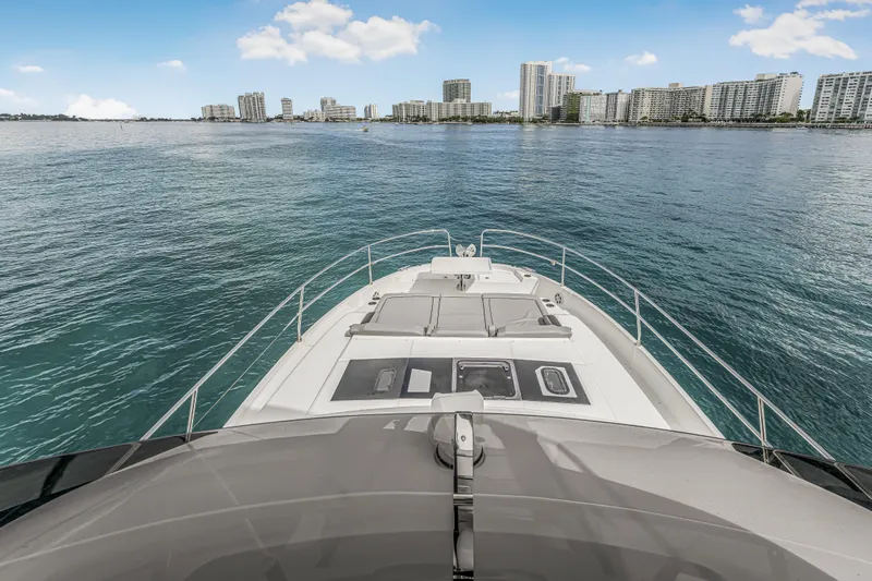 Rhapsody In Sea Yacht Photos Pics 2025 Jeanneau NC 1295 Fly yacht cruising near city skyline on calm waters.