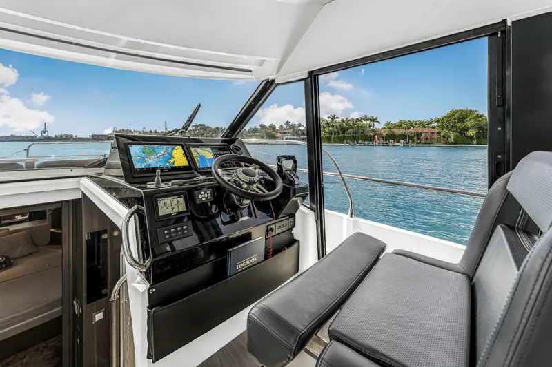 Rhapsody In Sea Yacht Photos Pics 2025 Jeanneau NC 1295 Fly cockpit with navigation screens, steering wheel, and waterfront view.