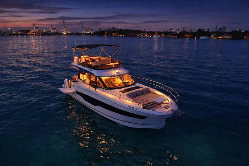 Rhapsody In Sea Yacht Photos Pics 2025 Jeanneau NC 1295 Fly yacht illuminated at sunset on calm waters.