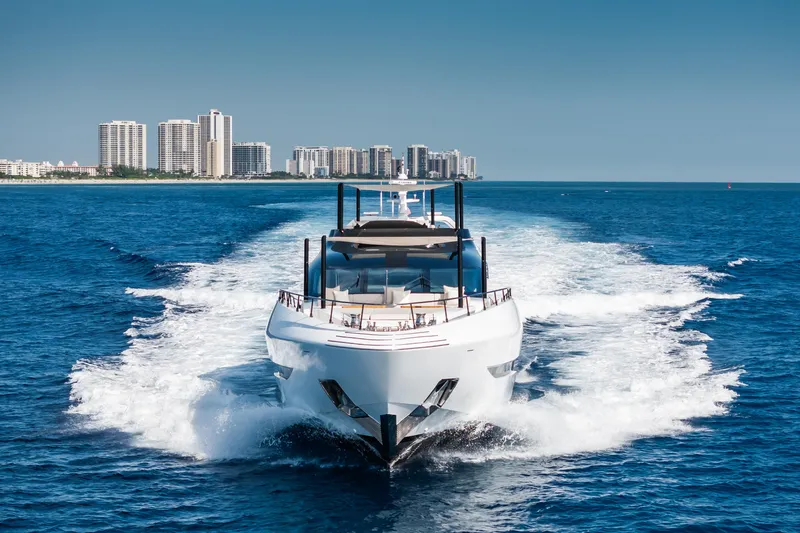  Yacht Photos Pics 2023 Mangusta 104 REV yacht cruising on blue ocean near city skyline.