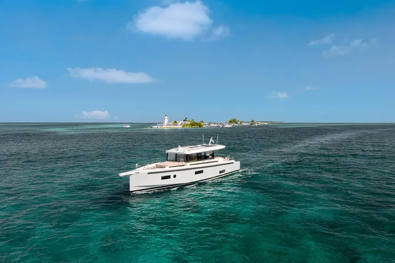  Yacht Photos Pics 2026 Omikron Yachts OT-60 cruising on clear blue ocean near tropical island.