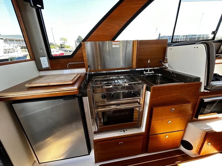 Silver Eagle Yacht Photos Pics 2024 Cutwater 32 Coupe NW Edition kitchen with stove, sink, fridge, and wooden cabinetry.