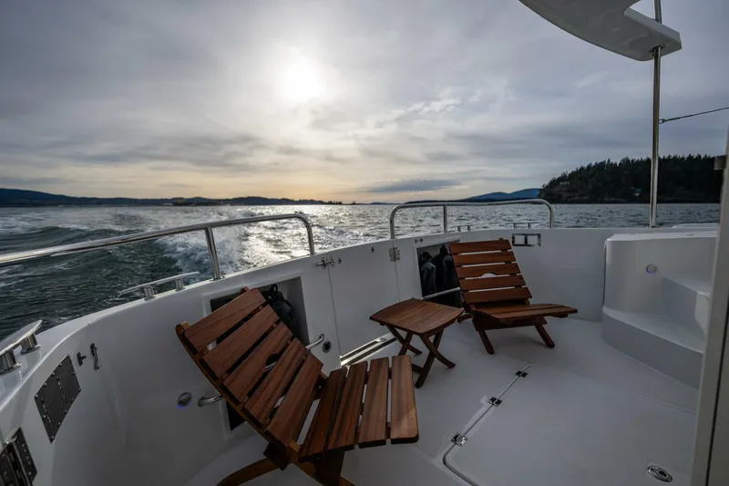 New Boat Hull #12 Yacht Photos Pics 2024 Nordic Tug 40 boat deck with wooden chairs, ocean view at sunset.