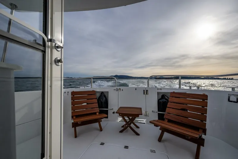 New Boat Hull #12 Yacht Photos Pics 2024 Nordic Tug 40 boat deck with wooden chairs, ocean view, and sunset.