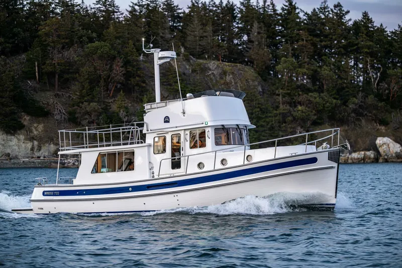 New Boat Hull #12 Yacht Photos Pics 2024 Nordic Tug 40 cruising on scenic waters near a forested shoreline.