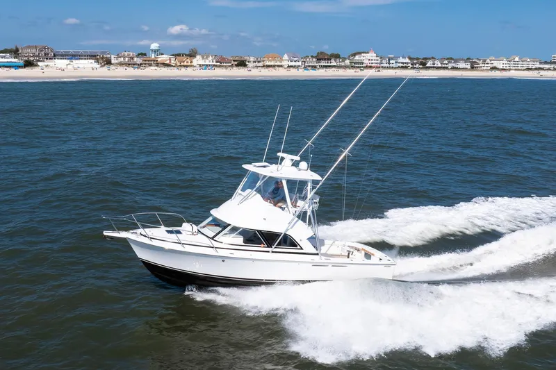 One More Yacht Photos Pics 2018 Bertram 35 Flybridge Sportfish cruising near a sandy beach with coastal buildings.
