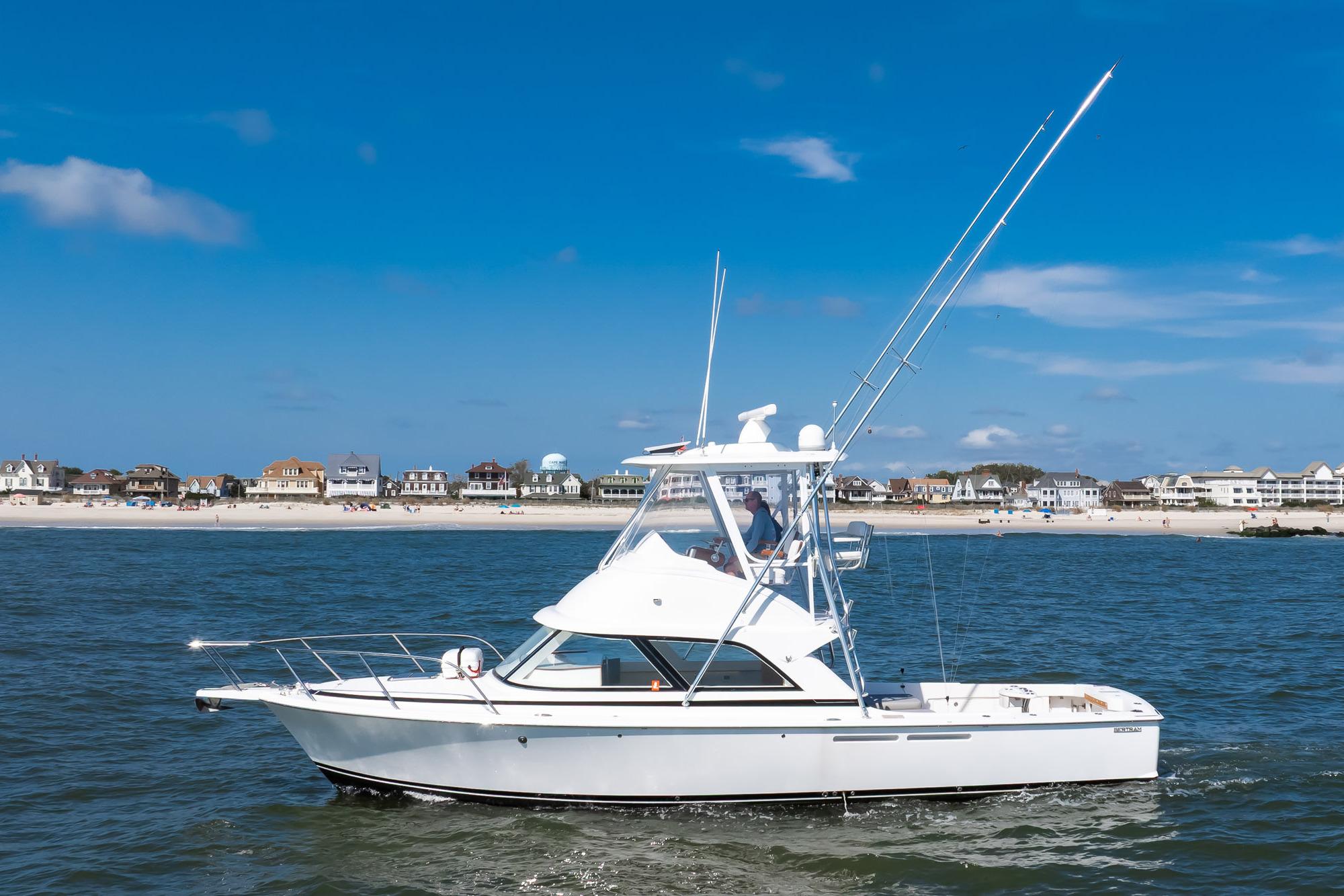 2018 Bertram 35 Flybridge Sportfish cruising near a sandy beach under a clear blue sky.