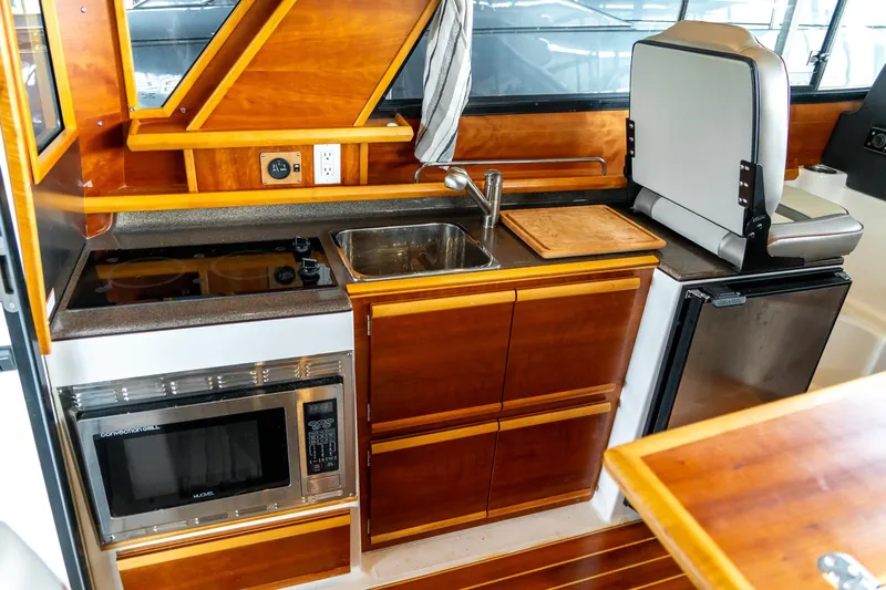  Yacht Photos Pics 2020 Cutwater C28 boat interior kitchen with wood cabinetry, sink, stove, microwave, and fridge.