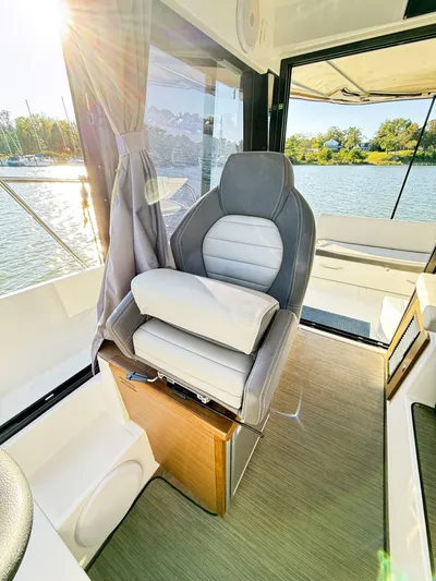  Yacht Photos Pics 2021 Jeanneau NC 895 boat interior with captain's chair, sunlit view, and water backdrop.