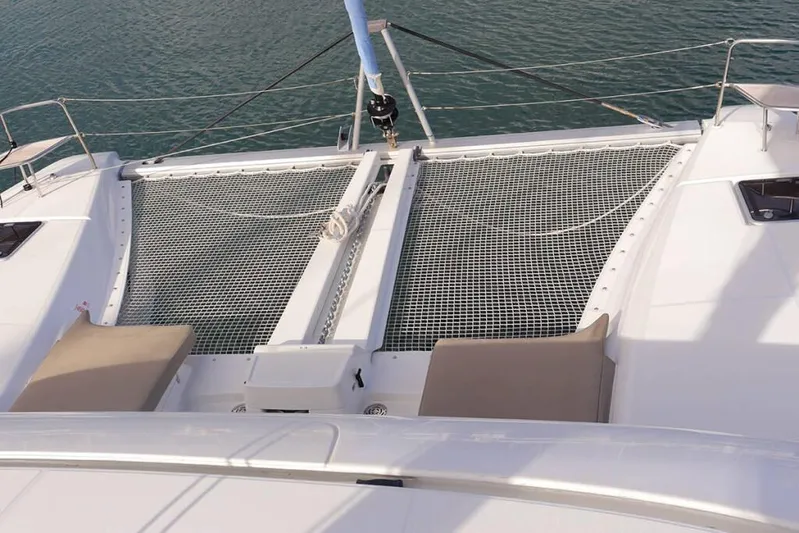  Yacht Photos Pics 2023 Lagoon 46 catamaran deck with netting and sun loungers on calm water.